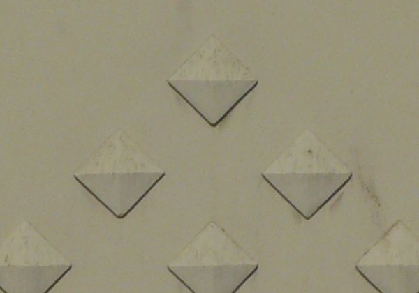 Concrete fence texture made up of a solid tan wall with a diamond pattern running through the middle, and a ball-topped stone column on either side. Rectangular recessions run along the top and bottom of the fence, and up the columns.